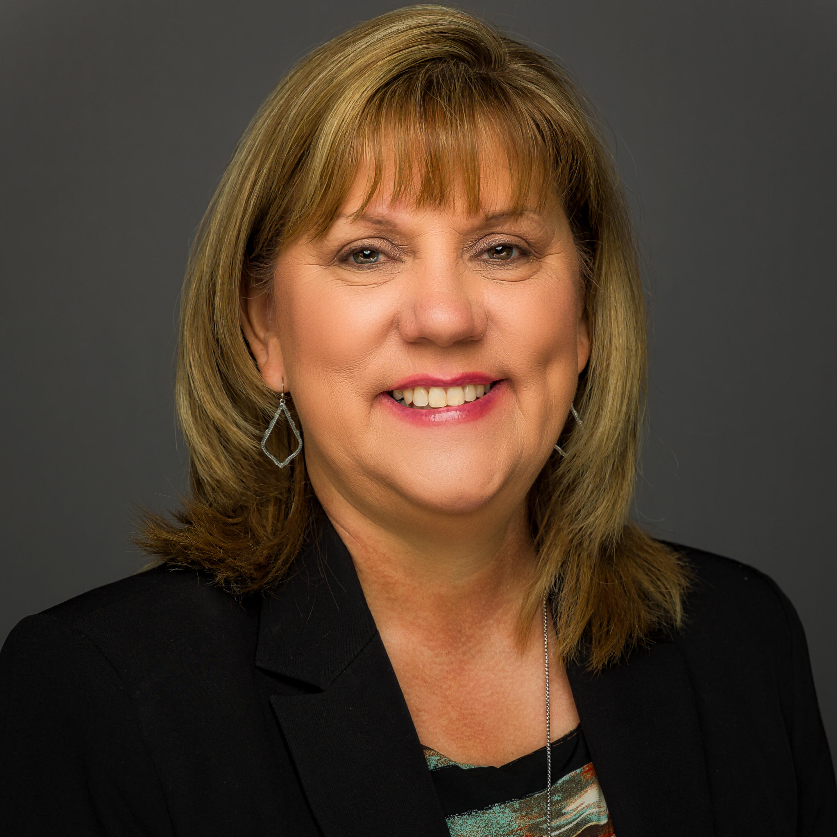 A professional headshot of a smiling woman posing against a dark gray background.