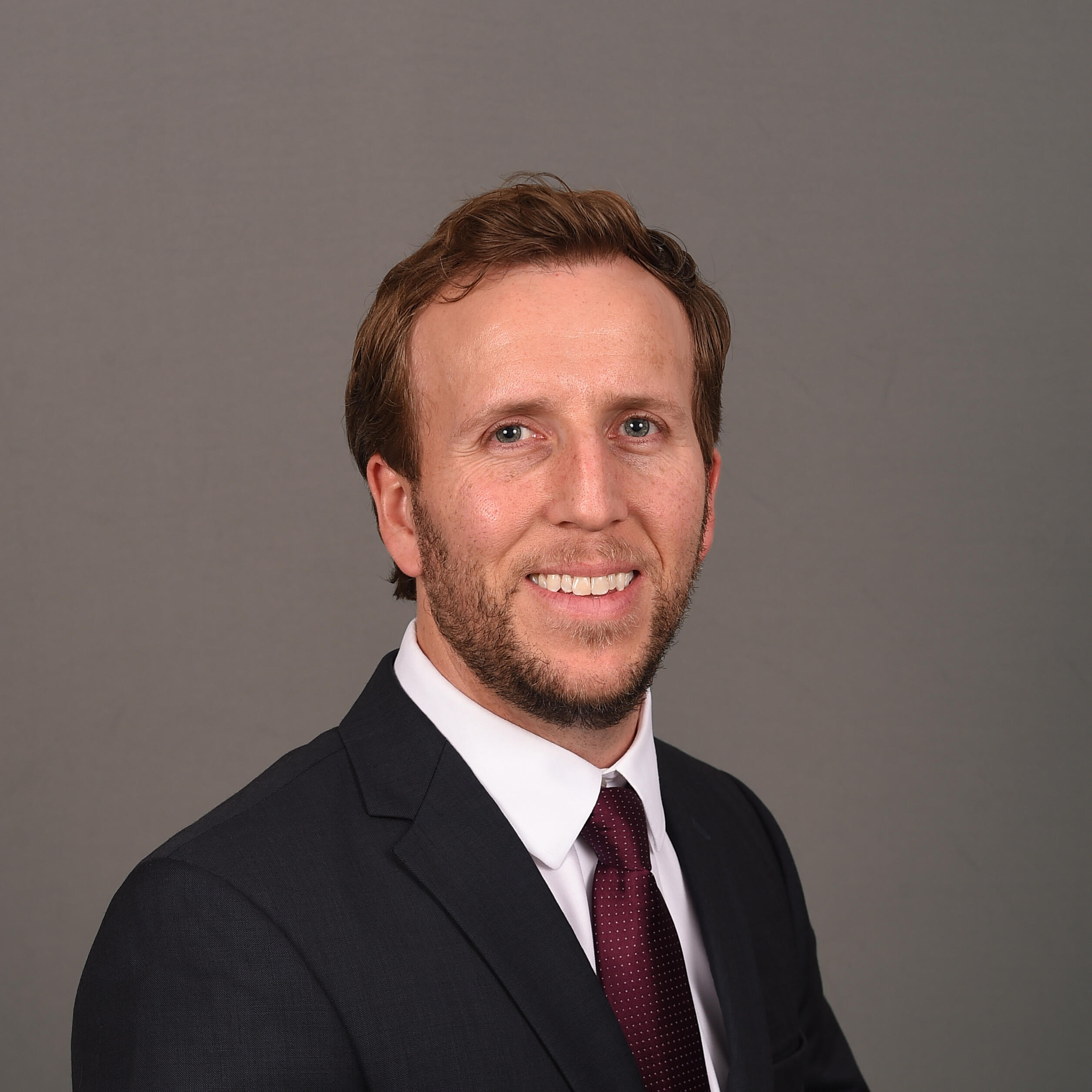 A person wearing a dark suit with a white dress shirt and a dark maroon tie.